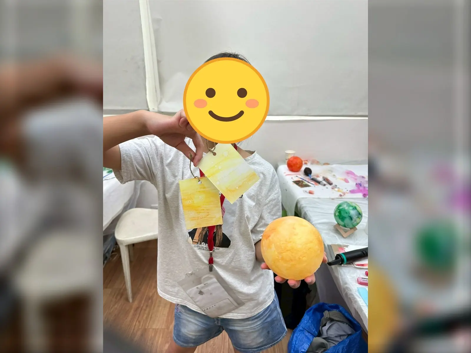 孩子展示兒童暑期繪畫課程完成的酒精墨水星球燈與書籤